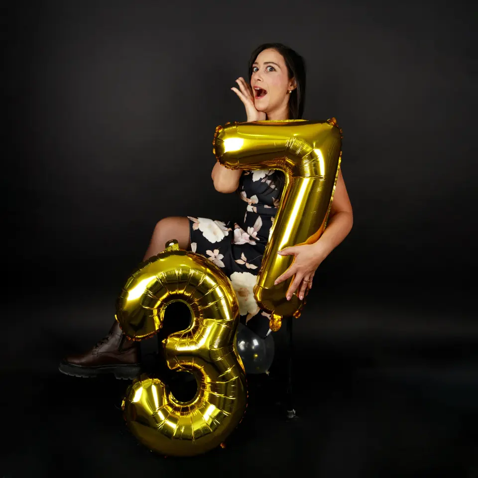 Femme posant avec des ballons dorés « 37 » sur fond noir