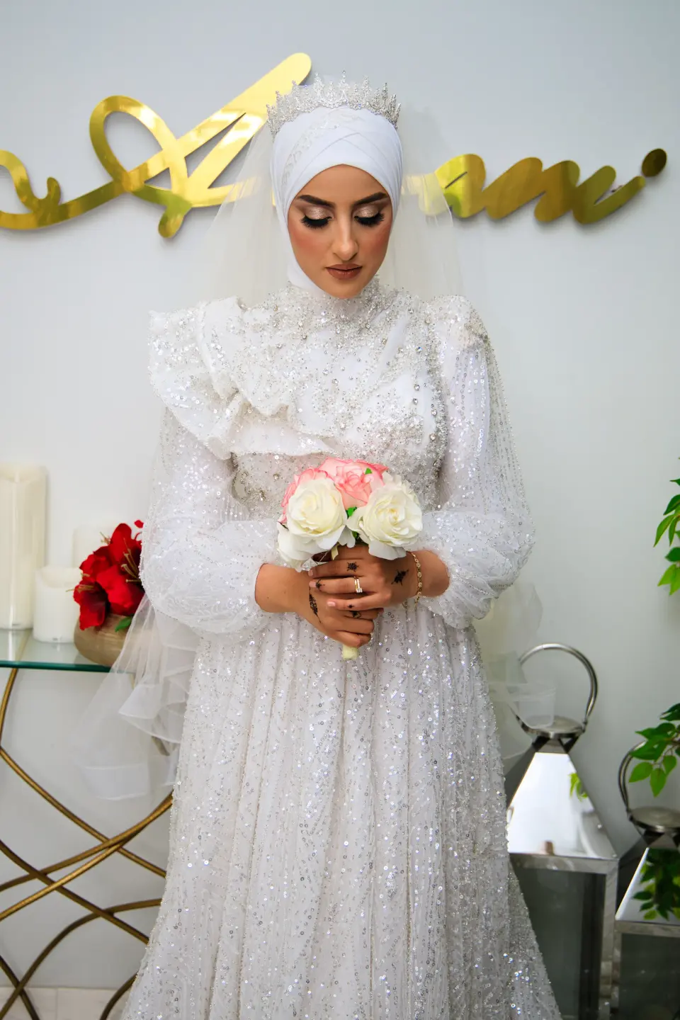 Mariée en robe blanche brodée tenant son bouquet devant un décor doré