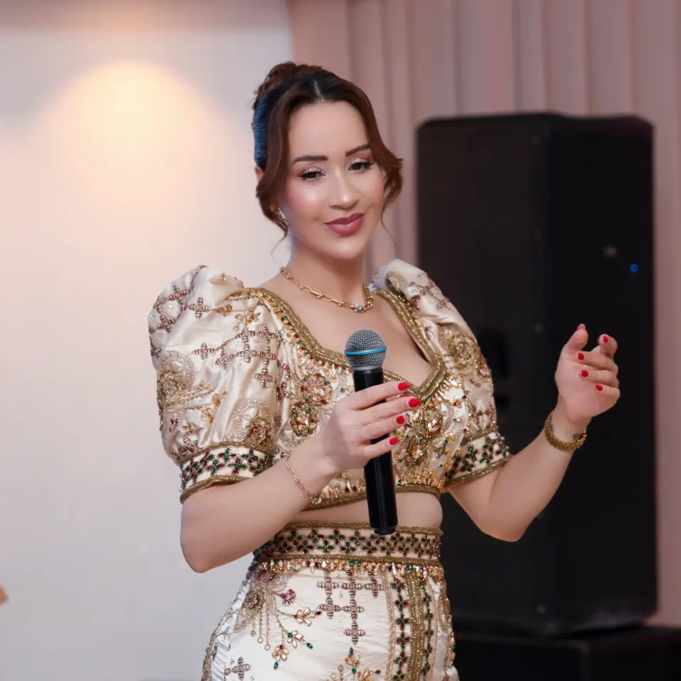 Femme en robe traditionnelle brodée chantant au micro lors d’un mariage